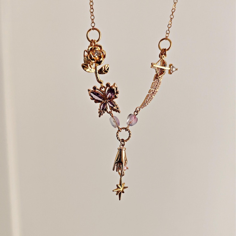 May include: A gold necklace with a variety of charms, including a rose, a butterfly, a hand, and a star. The charms are connected by a chain and beads.