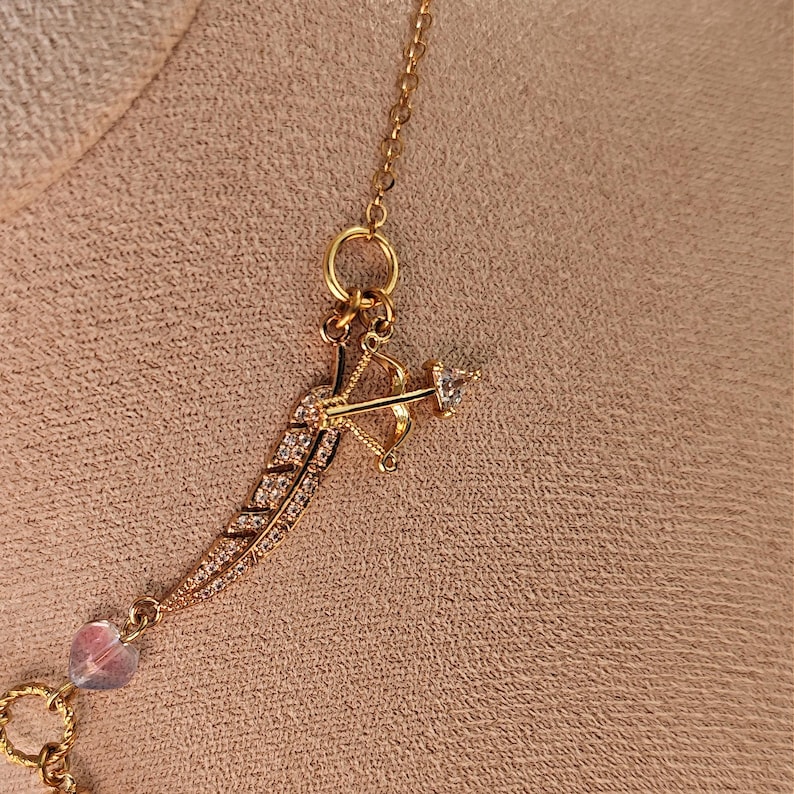 May include: A gold necklace with a feather charm and a small arrow charm. The charms are decorated with clear crystals.