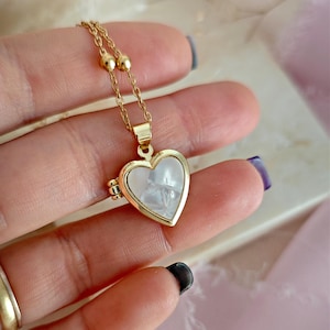 May include: A gold heart-shaped locket necklace with a white mother-of-pearl inlay. The locket has a hinged opening and a delicate chain.