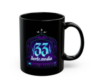 May include: A black ceramic mug featuring a graphic of a vintage radio silhouette in purple and blue tones. The design includes the number 33, the text hertz media, and radio dial knobs. The graphic is centered on the front of the mug.