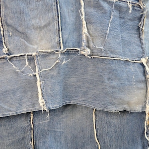 Puede incluir: Un primer plano de un mosaico de tela vaquera con bordes deshilachados. La tela es de color azul claro y se ha cosido en un patrón aleatorio.