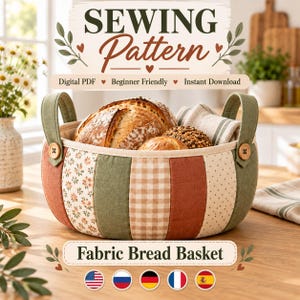May include: A round fabric bread basket featuring vertical panels in sage green, terracotta, and cream with floral, gingham, and polka dot patterns. The basket has two sage green handles attached with wooden buttons and contains several loaves of bread.