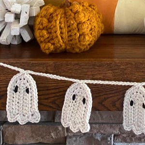 May include: A white crocheted ghost garland with black eyes, hanging on a wooden surface. The garland is perfect for Halloween decorations.