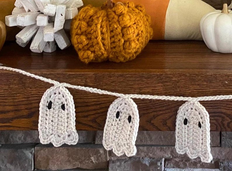 May include: A white crocheted ghost garland with black eyes, hanging on a wooden surface. The garland is perfect for Halloween decorations.