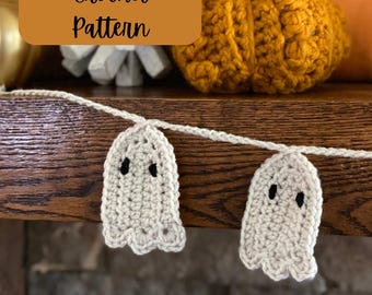 May include: A crochet garland with white ghost ornaments and black eyes. The garland is hanging on a wooden surface. The text "Crochet Pattern" is written on a brown rectangle.