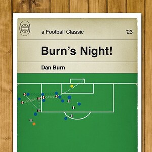 May include: A green and white football pitch with a football and players in blue and white kits. The text 'Burn's Night!' and 'Dan Burn' are printed on the poster. 'a Football Classic' and '23' are also printed on the poster.