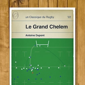 Könnte beinhalten: Eine Illustration eines grünen und weißen Rugbyfeldes mit einem weißen ovalen Ball, der durch die Torpfosten getreten wird. Der Text "Le Grand Chelem" befindet sich oben auf dem Bild, darunter der Text "Antoine Dupont". Der Text "un Classique du Rugby '22" befindet sich oben rechts auf dem Bild.