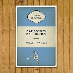 May include: A vintage-style book cover with a blue background and white text. The title is "Campeones del Mundo" with the subtitle "Argentina 2022". The cover also features a cartoon illustration of a soccer player kicking a ball.