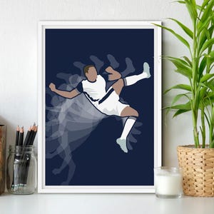 Op de afbeelding: Een ingelijste kunstdruk met een gestileerde illustratie van een voetballer die een bal schopt. De speler is afgebeeld in wit en marineblauw, met een bewegingssporeffect tegen een donkerblauwe achtergrond. De print wordt weergegeven op een wit oppervlak.