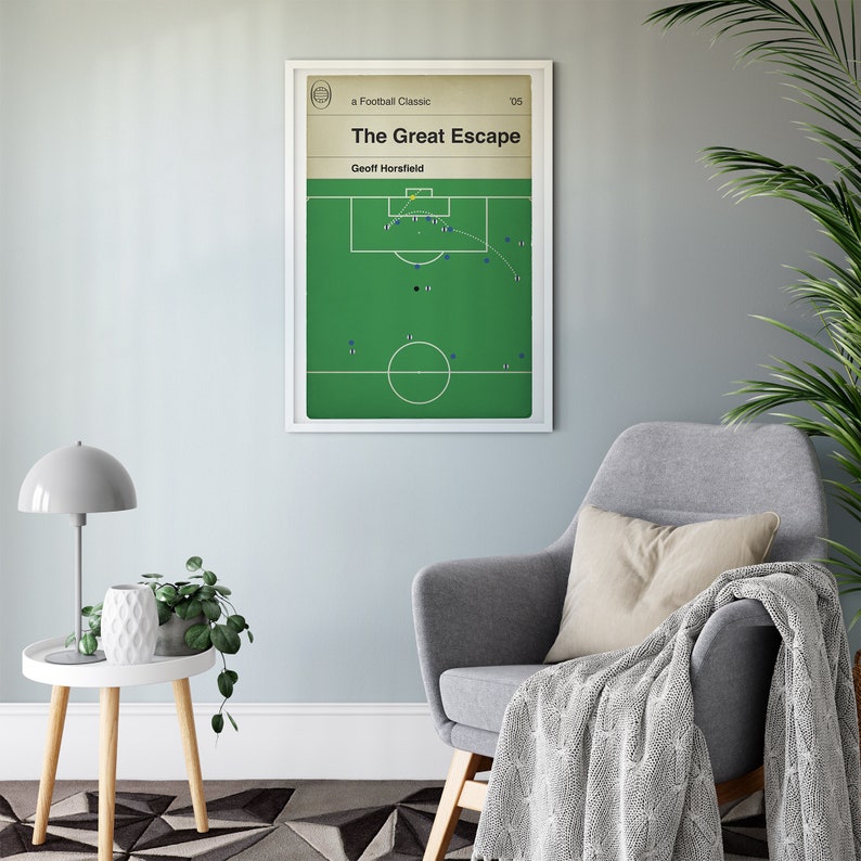 May include: A framed poster titled "The Great Escape" featuring a football play diagram. The poster has a white border and is displayed on a light blue wall. The room includes a gray armchair, a side table with a lamp, and a potted plant.