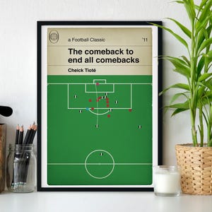 May include: A black framed print with a green soccer field and white lines. The text reads "a Football Classic '11 The comeback to end all comebacks Cheick Tioté".
