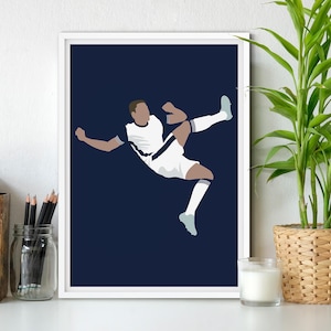 Op de afbeelding: Een ingelijste kunstdruk met een gestileerde illustratie van een voetballer in actie, die een bal trapt. De speler draagt een wit uniform met marineblauwe accenten tegen een marineblauwe achtergrond. De print wordt op een witte muur getoond.