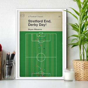 May include: A framed print titled "Stretford End, Derby Day!" featuring a football field diagram. The top section has text on a tan background. The field is green with player positions marked by dots and lines.