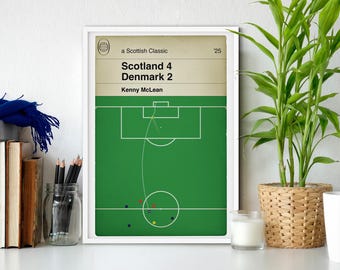 Puede incluir: Un estampado enmarcado que presenta un diagrama de campo de fútbol con el texto "Scotland 4 Denmark 2" y "Kenny McLean". El estampado tiene un campo verde, un marco blanco y un fondo beige. También se ven una planta en una cesta tejida y una taza blanca.