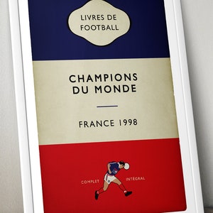 May include: A vintage-style book cover with a blue, white and red colour scheme. The title reads "Champions du Monde" with the text "France 1998" below. The cover features a football player in a blue jersey running with a football. The words "Complet" and "Integral" are at the bottom of the cover.