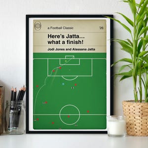 以下が含まれることがあります： 緑色のサッカーフィールドの図、白い線、選手の位置が描かれた額入りポスター。テキストには「a Football Classic '26, Here's Jatta... what a finish!, Jodi Jones and Alassana Jatta」と記されています。点線はボールの軌道を示しています。