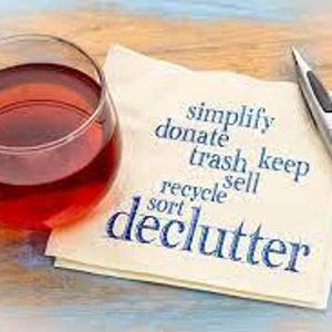 May include: A clear glass mug filled with red liquid, a beige paper napkin printed with the words simplify, donate, trash, keep, sell, recycle, sort, and declutter in blue, and a silver ballpoint pen with a black grip.