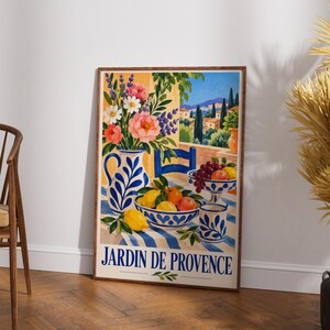 May include: A rectangular wall art print titled JARDIN DE PROVENCE featuring a colorful illustration of a table set with a blue and white patterned pitcher, bowls of fruit, and a bouquet of flowers against a Mediterranean landscape.