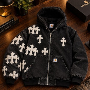 May include: A black denim zip-up hooded jacket featuring white cross-shaped patches across the front and sleeves. The jacket includes a Carhartt brand label on the chest and inside the collar, a front zipper closure, and a black fleece lining.