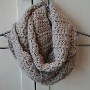 May include: A brown crocheted infinity scarf hanging on a hanger.