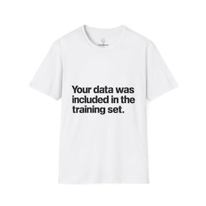 Pode incluir: Uma t-shirt branca de manga curta com o texto preto "Your data was included in the training set." impresso no peito. A etiqueta interior do pescoço apresenta um pequeno logótipo circular com uma cara sorridente e o texto "CasualDread".