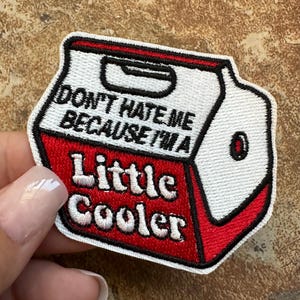 May include: White and red embroidered iron-on patch shaped like a small cooler with the text "Don't hate me because I'm a little cooler".