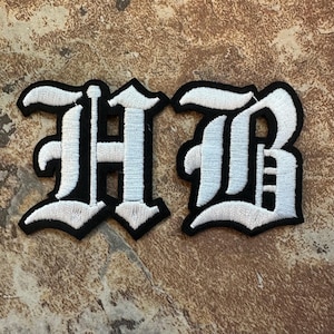 May include: White embroidered iron-on patch with the letters "HB" in a gothic font.