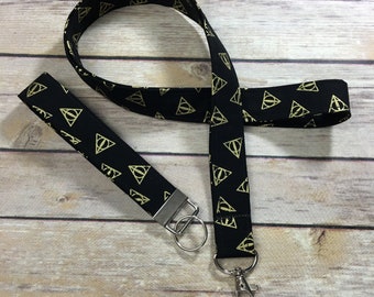 May include: Black and gold lanyard with a repeating pattern of the Deathly Hallows symbol. The lanyard has a silver key ring and a silver clip.