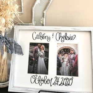 Op de afbeelding: Een wit fotokader met twee trouwfoto's. De namen "Calvin & Chelsie" en de datum "24 oktober 2020" zijn in zwart schrift geschreven. Het frame wordt ondersteund door een zwarte metalen standaard.