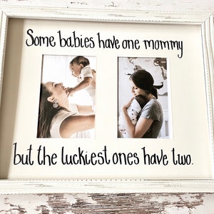 May include: A white distressed wooden picture frame containing two vertical photographs and the black text Some babies have one mommy but the luckiest ones have two. The left photo shows a person holding a baby, and the right shows a person holding a baby.