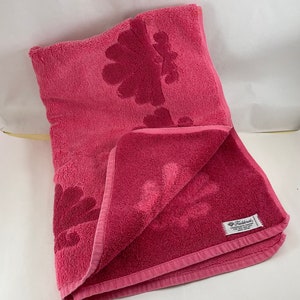 May include: A pink bath towel with a floral design and a Fieldcrest brand label. The towel is folded in half and has a textured surface.