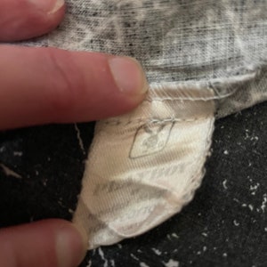 Peut inclure: Une &eacute;tiquette en tissu blanc avec du texte noir. L'&eacute;tiquette est attach&eacute;e &agrave; un v&ecirc;tement. Le texte sur l'&eacute;tiquette est partiellement obscurci.