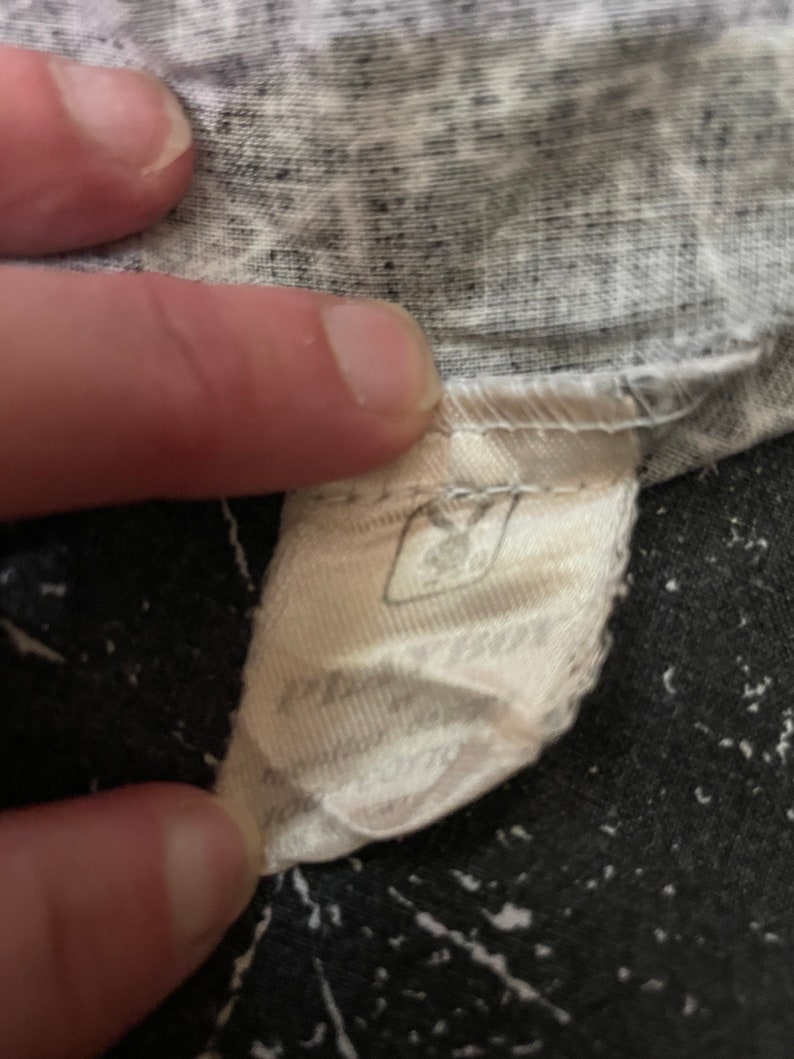 Peut inclure: Une &eacute;tiquette en tissu blanc avec du texte noir. L'&eacute;tiquette est attach&eacute;e &agrave; un v&ecirc;tement. Le texte sur l'&eacute;tiquette est partiellement obscurci.