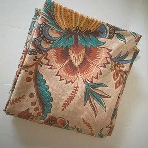May include: A beige fabric with a floral pattern in shades of brown, teal, and yellow. The fabric features a large floral design with intricate details.