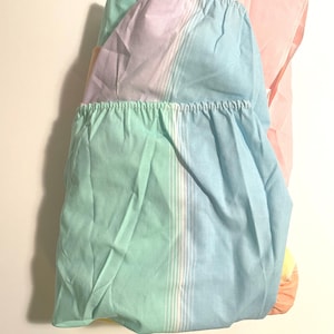 Puede incluir: Una sábana bajera doblada con un patrón de rayas arcoíris en tonos de rosa, amarillo, verde y azul.