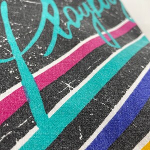 Peut inclure: Tissu noir avec un motif ray&eacute; turquoise, rose, bleu et jaune. Le mot "Royal" est &eacute;crit en lettres cursives turquoise.