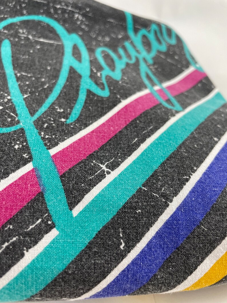 Peut inclure: Tissu noir avec un motif ray&eacute; turquoise, rose, bleu et jaune. Le mot "Royal" est &eacute;crit en lettres cursives turquoise.