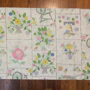 Peut inclure: Tissu de coton blanc avec un motif répété de fleurs colorées, de paniers et de roues. Le motif est cousu en point de croix.