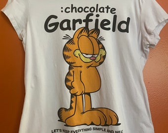 May include: White t-shirt with a cartoon image of Garfield the cat. The text ':chocolate Garfield' is printed above the image and the text 'LET'S KEEP EVERYTHING SIMPLE AND NEAR' is printed below the image.