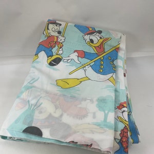 Puede incluir: Una sábana de algodón azul y blanca con un estampado de personajes de Disney, incluyendo a Donald Duck, Mickey Mouse y Minnie Mouse. Los personajes están vestidos con atuendos rojos, azules y amarillos.