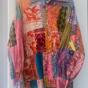 May include: A patchwork button-down shirt with a collared neckline. The shirt features a variety of colorful fabric squares with floral and geometric patterns. The shirt is hanging on a hanger against a white background.