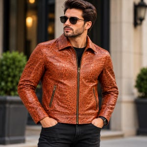 May include: A tan, textured leather jacket with a crocodile-skin pattern, featuring a pointed collar, a full-length front zipper, and two zippered side pockets. The jacket is worn over a black shirt and paired with black pants.
