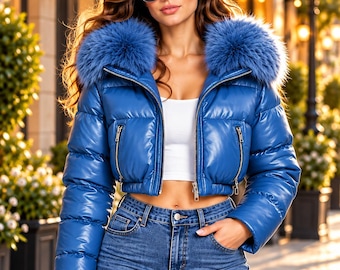 Puede incluir: Una chaqueta acolchada corta de color azul brillante con un cuello grande de piel sintética azul, mangas largas y dos bolsillos delanteros con cremallera. La chaqueta se lleva sobre un top corto blanco y vaqueros azules, con gafas de sol tipo aviador.