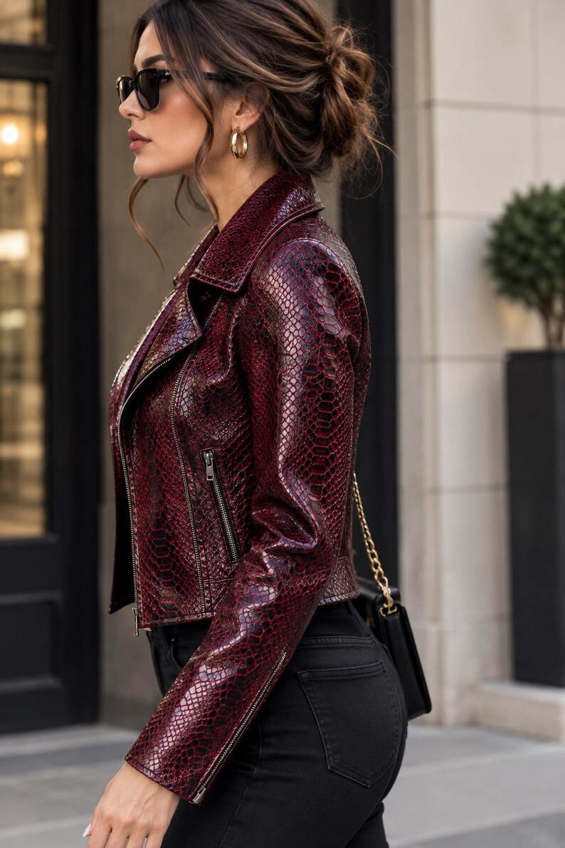 Puede incluir: Una chaqueta de motorista color burdeos intenso con un patr&oacute;n texturizado de piel de serpiente, cuello de solapa y cremalleras met&aacute;licas plateadas en la parte delantera y las mangas. La chaqueta se combina con pantalones negros y un bolso peque&ntilde;o.
