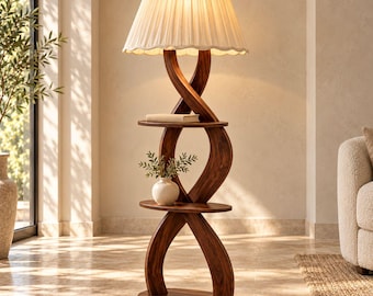 Peut inclure: Un lampadaire doté d'une base en bois brun foncé avec deux supports incurvés entrelacés et deux étagères ovales. La lampe est surmontée d'un abat-jour en tissu blanc cassé plissé avec un bord festonné, diffusant une lumière chaude.