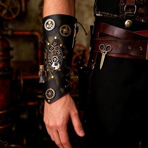 May include: A black leather forearm bracer adorned with metallic gears, a central diamond-shaped gear assembly, and a small glass vial. A brown leather belt with a gold-toned scissor charm is worn around the waist over black trousers.