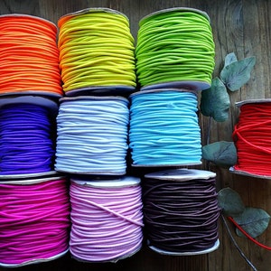 May include: Ten spools of colourful elastic cord, each wound around a white cardboard spool. The colours are orange, yellow, green, blue, purple, white, pink, light pink, brown, and red.
