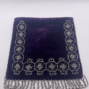May include: A deep purple velvet bag with intricate silver beaded detailing. The bag features a beaded border and a fringe of silver beads along the bottom edge. The design is symmetrical and elegant.