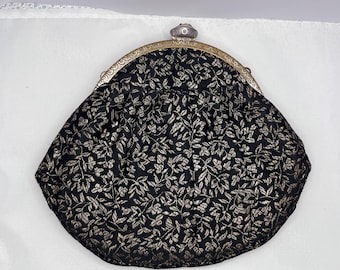 May include: Black and gold floral patterned clutch with a silver clasp. The vintage purse features a rounded shape and a decorative metal frame. The fabric has a repeating leaf design.