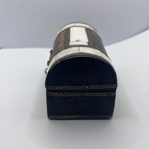 May include: A small, antique wooden chest with a rounded top. The chest is dark brown with white and silver accents. The lid and base are rectangular, and the sides are curved. The chest is likely used for storing small items.